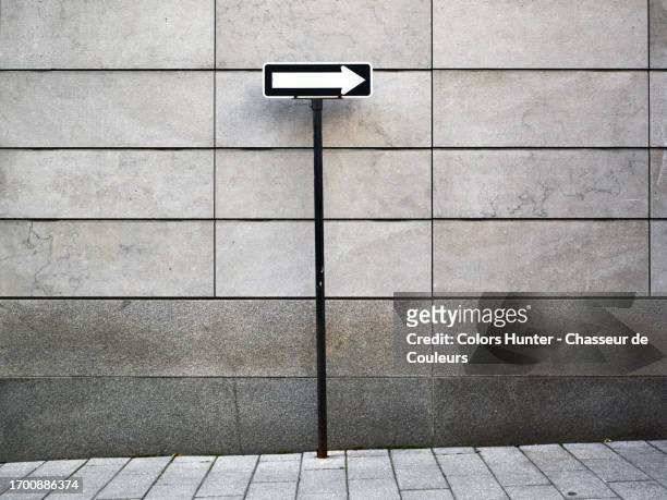 close-up of a road sign with an arrow on a pole in front of a gray stone wall and sidewalk in montreal, quebec, canada - sign pole stock pictures, royalty-free photos & images