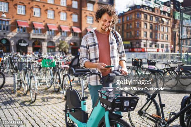male tourist renting a bike in the city - bicycle parking station stock pictures, royalty-free photos & images