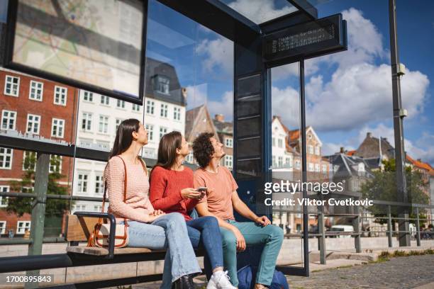 three caucasian friends sitting at the bus station waiting for the bus - bus denmark stock pictures, royalty-free photos & images