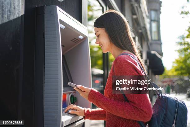 mujer caucásica retirando dinero en el cajero automático al aire libre - cajero fotografías e imágenes de stock