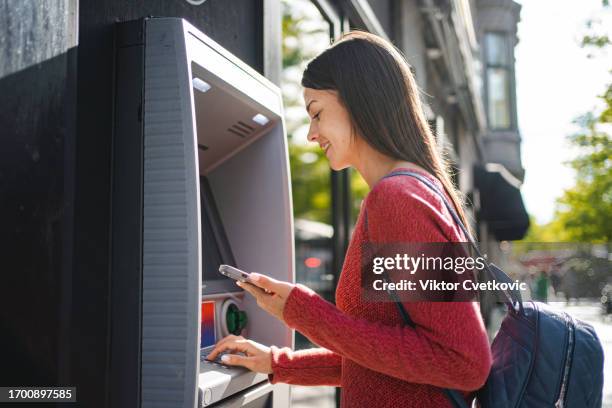 caucasian woman withdrawing money at the outdoor atm machine - atm stock pictures, royalty-free photos & images