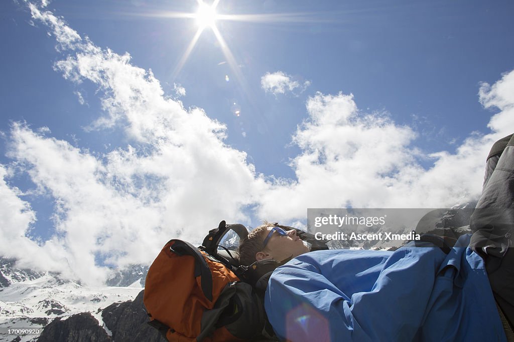 Hiker relaxes against backpack, snowy mountains