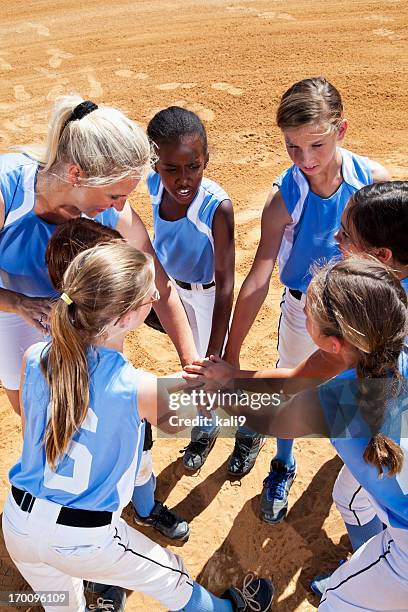 softball players with coach in huddle doing team cheer - softball sport stock pictures, royalty-free photos & images