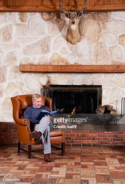 senior man reading by fireplace - sitting by fireplace stock pictures, royalty-free photos & images