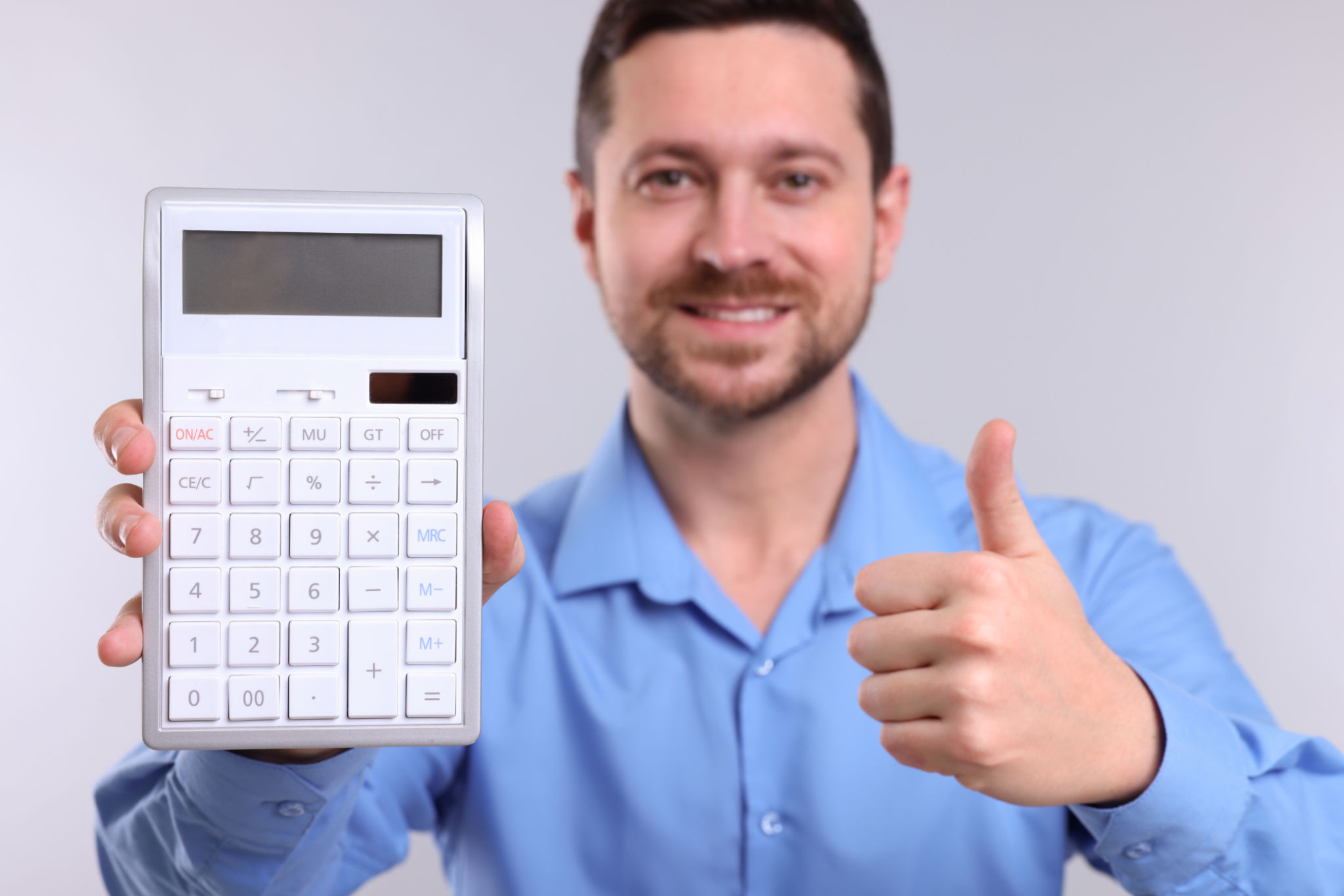 Happy accountant with calculator showing thumbs up on light grey background, selective focus Happy accountant with calculator showing thumbs up on light grey background, selective focus