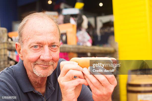 smiling senior man with a hotdog - man eating a hot dog stock pictures, royalty-free photos & images