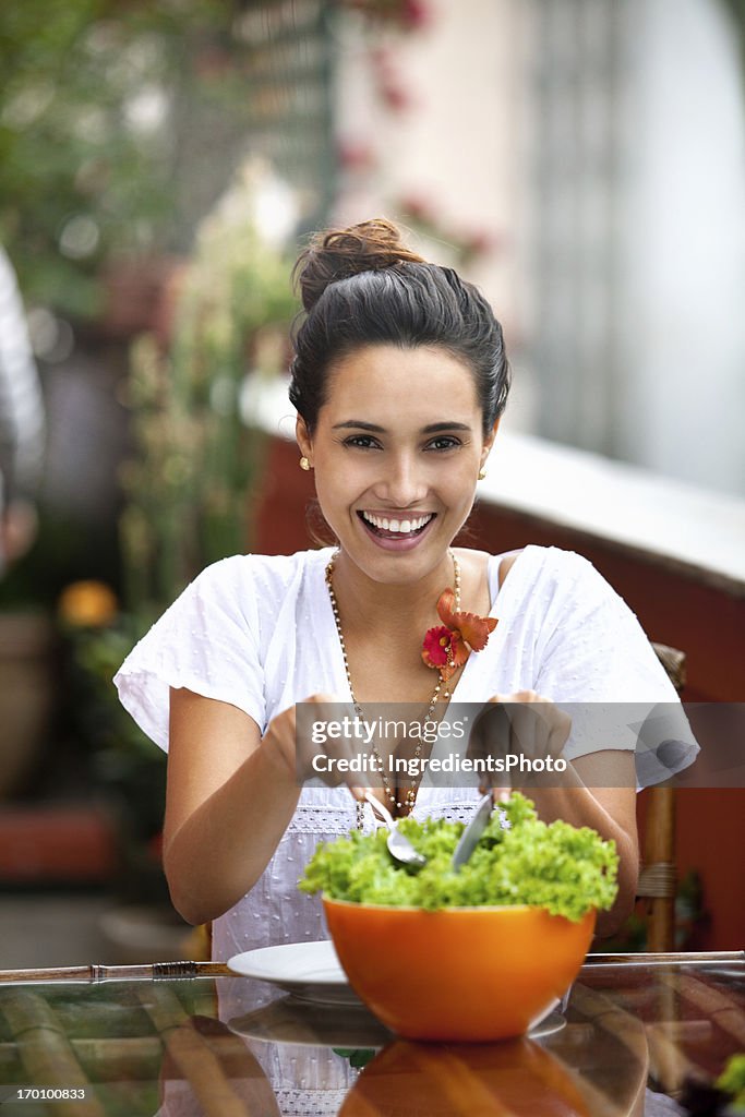 Young and beautiful smiling woman eating salad on the table.