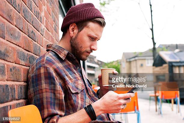 young male adult checking his smart phone sitting outside a trendy cafe - mid adult men stock pictures, royalty-free photos & images