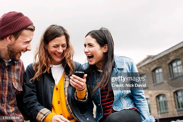 friends laughing together looking at content on a smart phone - phone a friend stock pictures, royalty-free photos & images