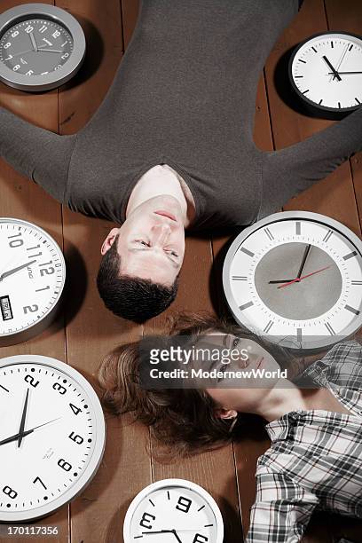 young male and female lying on floor with clocks - 24 hours stock-fotos und bilder
