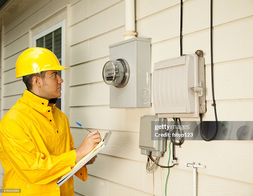 Electrician, repairman at outside electric meter on home. Yellow raincoat.