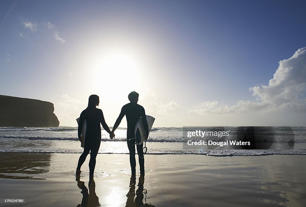 Silhouette of couple holding hands at beach.