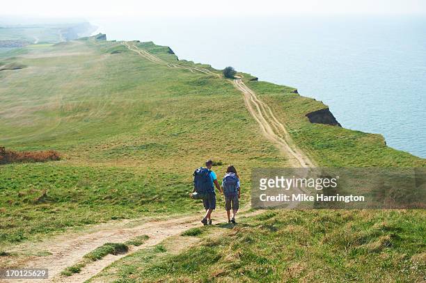 male and female walking along path on cliff top - costa caratteristica costiera foto e immagini stock