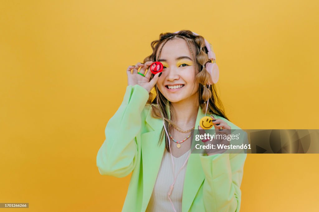 Smiling woman with headphones holding smileys against yellow background