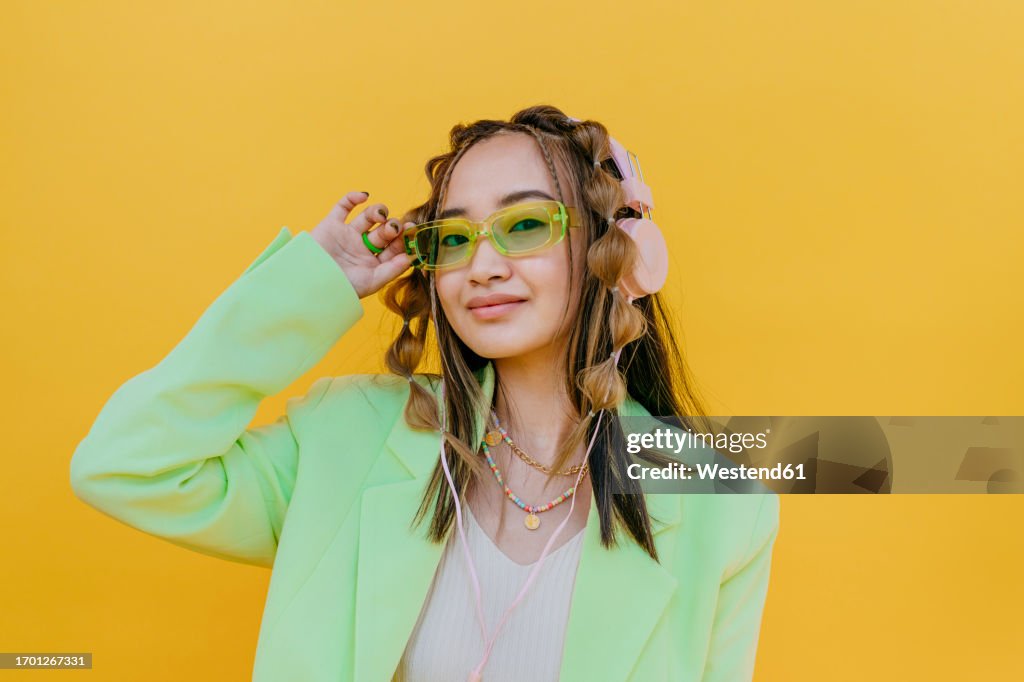 Young woman wearing sunglasses and listening music through headphones in studio