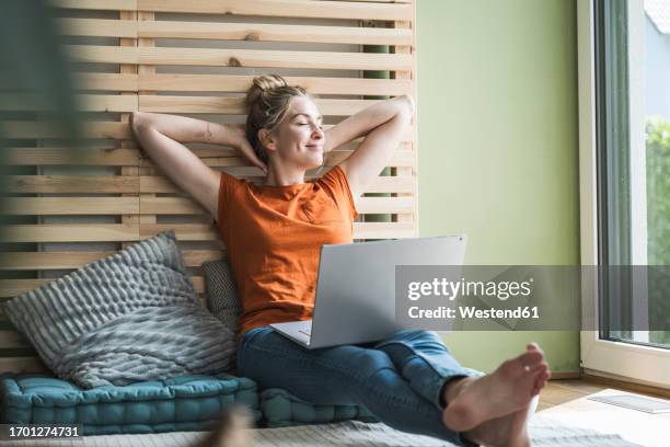 portrait of woman sitting on mattress relaxing with laptop - hands behind head stock pictures, royalty-free photos & images