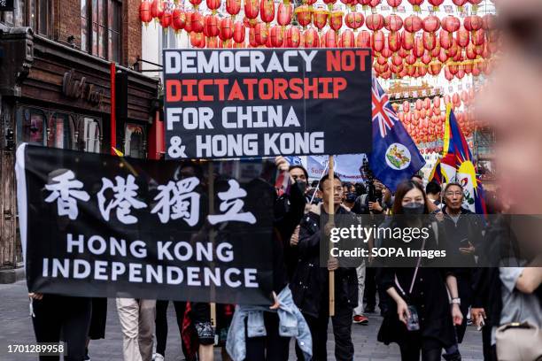 Protesters are seen holding a huge placard and a flag supporting the independence of Hong Kong while marching in Chinatown in London during the joint...