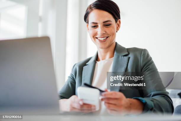 smiling businesswoman using credit card in workplace - lecteur de carte de crédit photos et images de collection