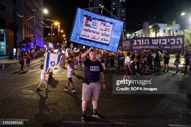 Protester holds a placard with the Israeli and Palestinian flag that reads 'peace now' next to a black sign that reads 'occupation kills' during a...