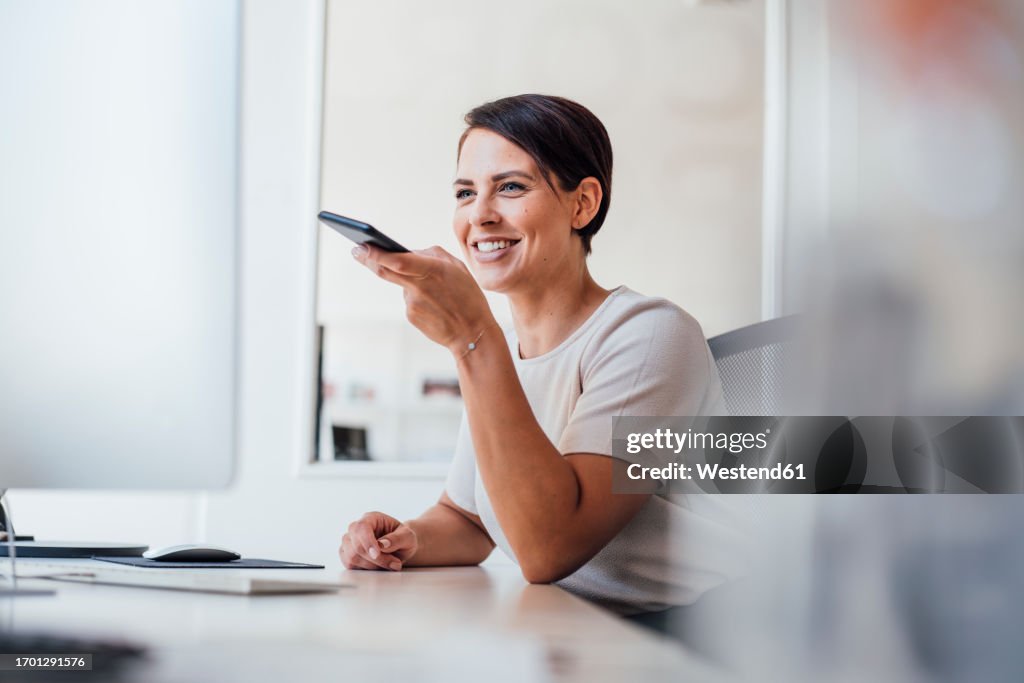 Happy businesswoman sending voicemail on smart phone
