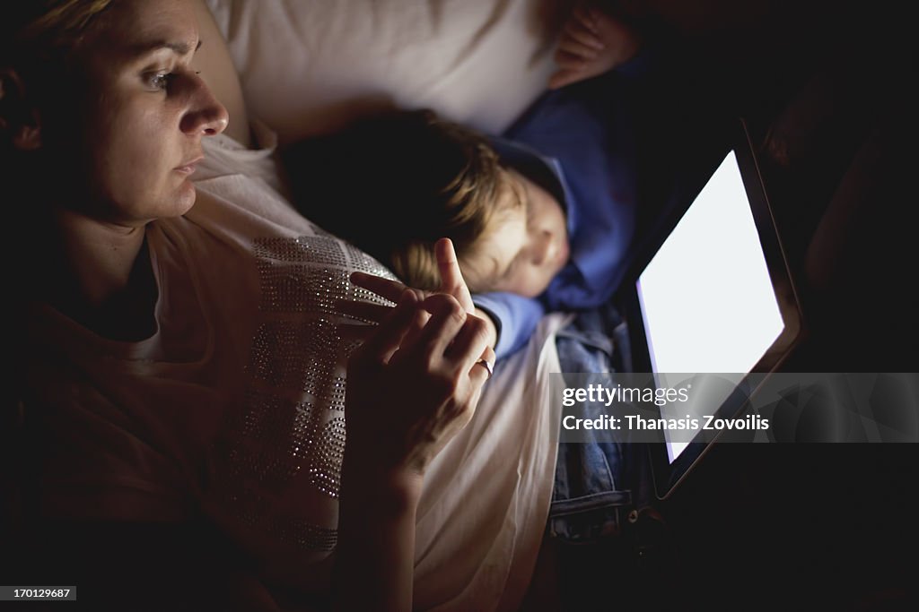 Mother with son looking at a tablet in the dark