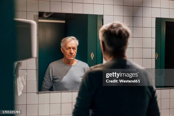 senior man looking in mirror in bathroom - mirror fotografías e imágenes de stock