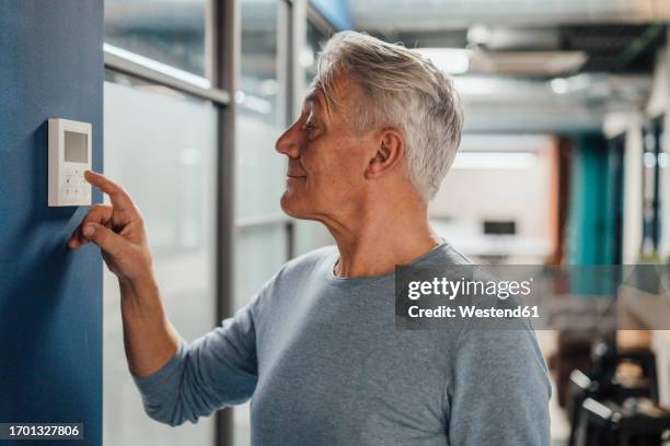 smiling senior businessman using digital thermostat at work place - office thermostat stock pictures, royalty-free photos & images