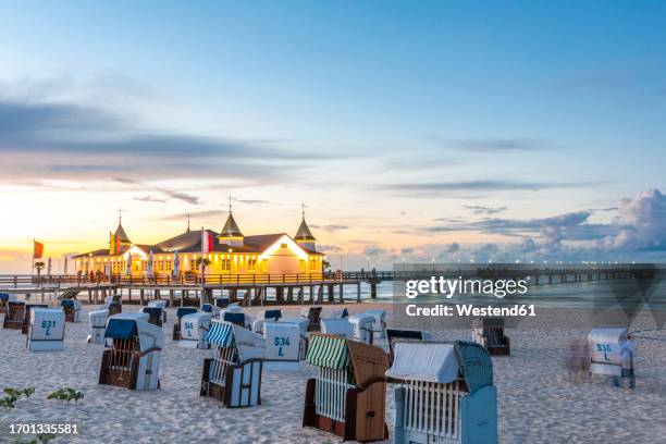 germany, mecklenburg-vorpommern, ahlbeck, hooded beach chairs at sunset with pier and bathhouse in background - ahlbeck stock pictures, royalty-free photos & images