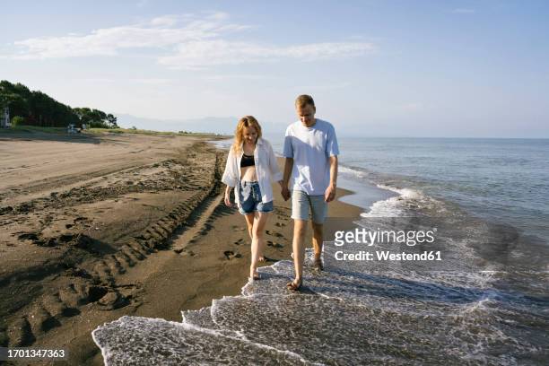 couple walking barefoot at beach on sunny day - georgia love fotografías e imágenes de stock