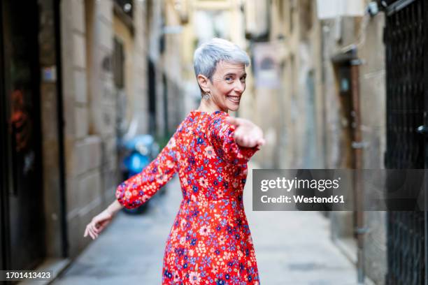 smiling woman wearing red dress beckoning in alley - inviting gesture stock pictures, royalty-free photos & images