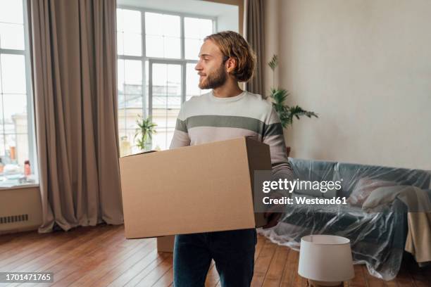 young man with cardboard box standing in living room - man wrapped in plastic stock pictures, royalty-free photos & images