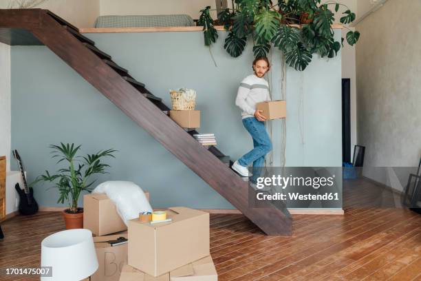 young man moving down with cardboard box on staircase - descending a staircase stock pictures, royalty-free photos & images