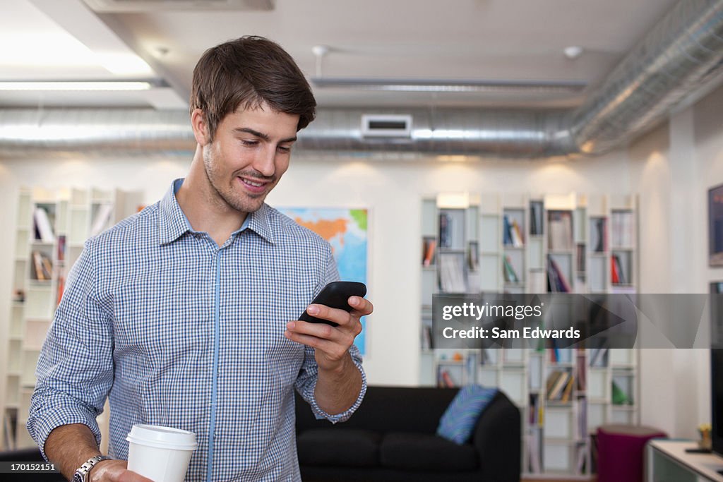 Portrait of smiling businessman using cellphone with coffee cup in office