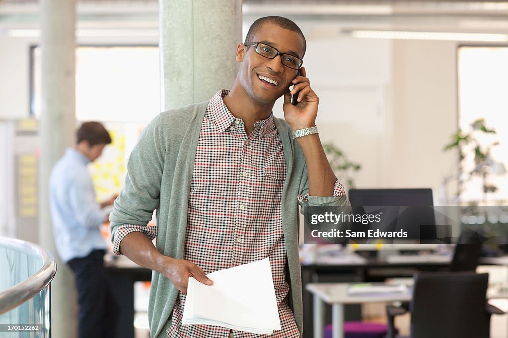 Businessman with paperwork talking on cell phone in office