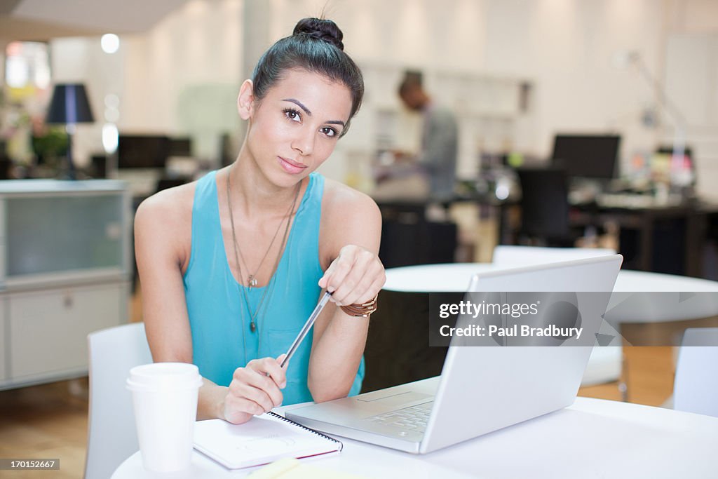 Businesswoman with laptop writing on notepad in office