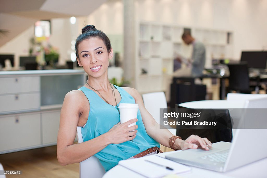 Portrait of smiling businesswoman drinking coffee at laptop in office