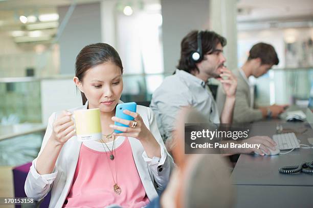 businesswoman drinking coffee and text messaging with feet up in office - tijd verspillen stockfoto's en -beelden