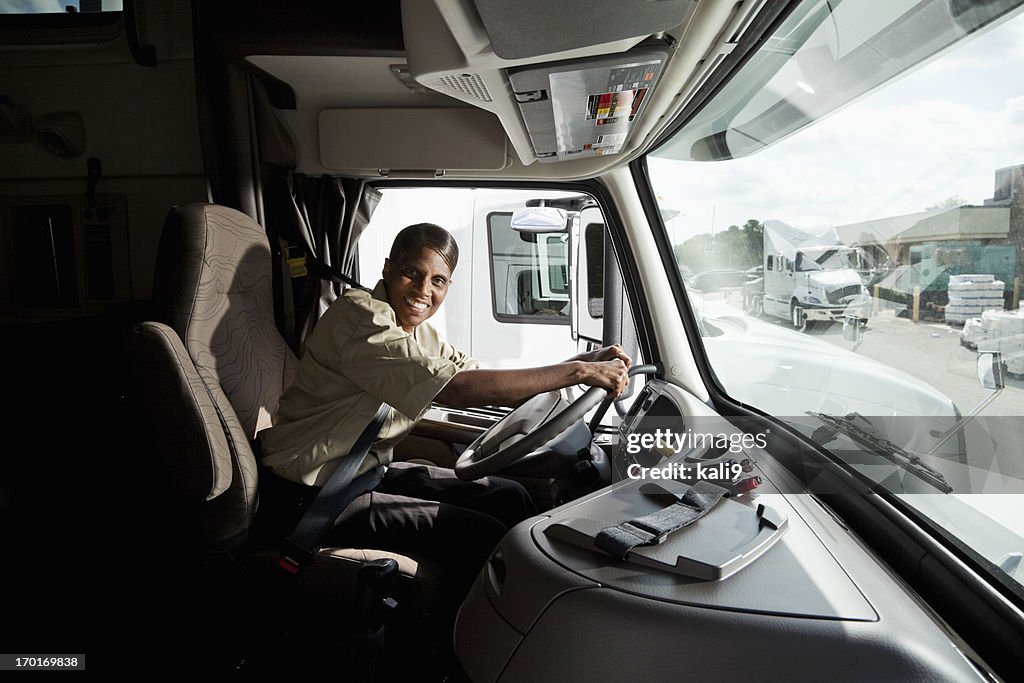 Female truck driver sitting in cab of semi-truck