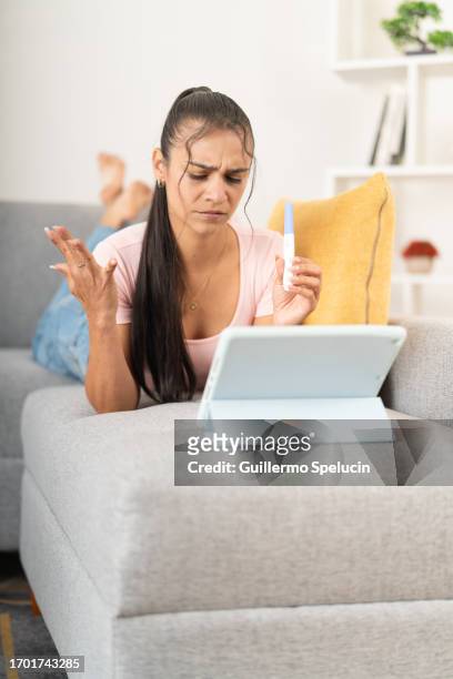 disappointed young woman with her positive pregnancy test figuring out what to do on her tablet - surprised woman looking at tablet stock pictures, royalty-free photos & images