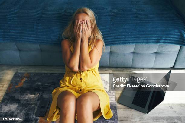 a young woman is sitting on the floor, covering her face with her hands, with a laptop - abuse bildbanksfoton och bilder