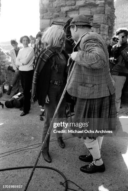 French actress Brigitte Bardot, with a tartan scarf wrapped around her neck, and British actor James Robertson Justice, who wears a tweed...