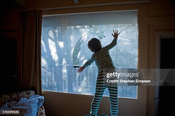 boy in pajamas playing with condensation on window - condensation stock pictures, royalty-free photos & images