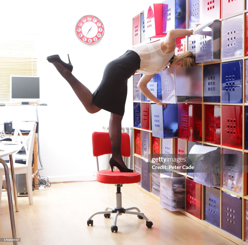 Woman stood on chair looking in storage shelves