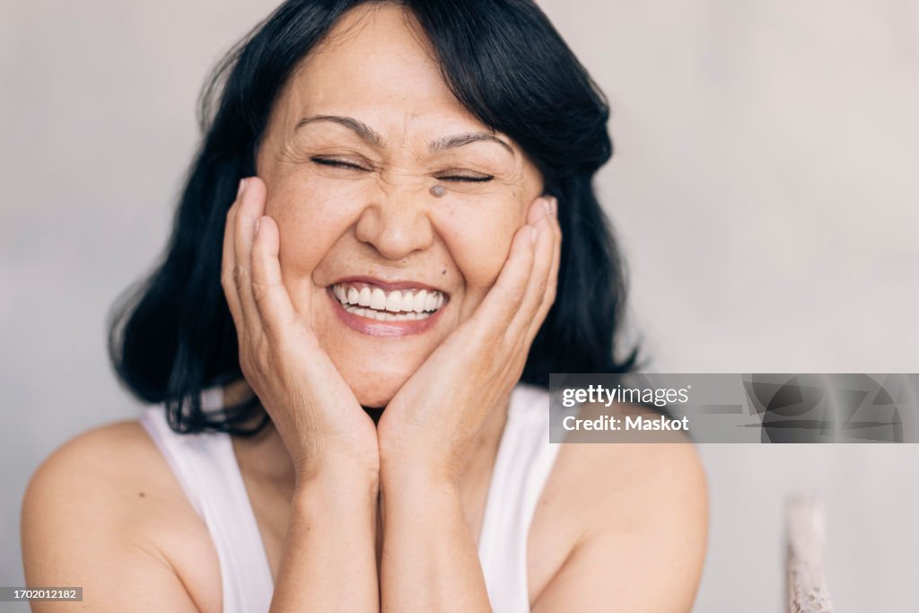Happy mature woman touching face against white background