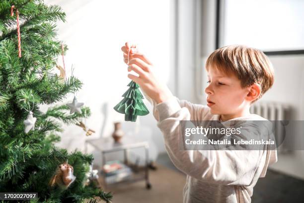 christmas tree decor: boy child adds green paper ornaments, eco-friendly. - décembre photos et images de collection