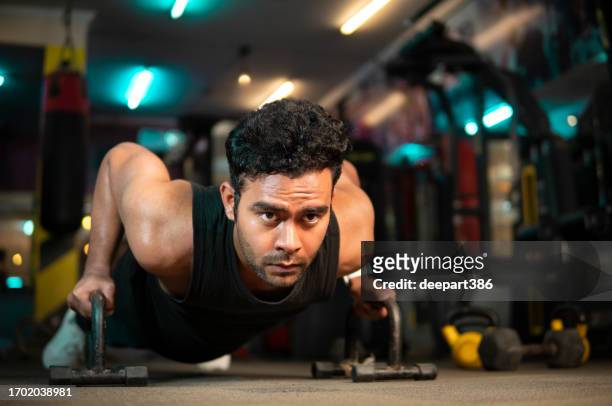 strong muscular young man doing push-up bars exercise at the gym. - sports india stock pictures, royalty-free photos & images