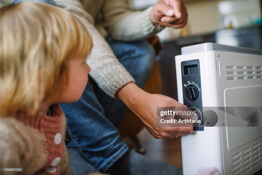 Familie wärmt die Hände zu Hause über einem tragbaren Heizkörper / Heizkörper im kalten Winter