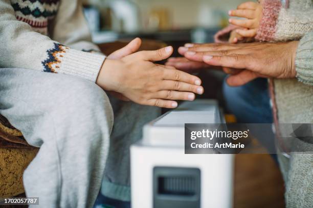 family warming hands at home over a domestic portable radiator/heater in cold winter - electric fire stock pictures, royalty-free photos & images