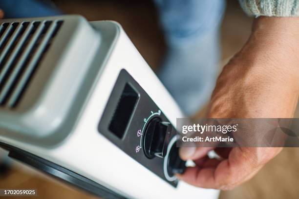 man turning on a domestic portable radiator/heater in cold winter - electric fire stock pictures, royalty-free photos & images