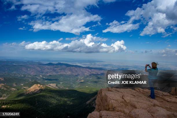 Woman takes a picture at the top of Pikes Peak mountain in the Front Range of the Rocky Mountains within Pike National Forest, 10 miles west of...